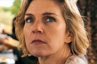 Rhea seehorn s carol looking seriously over her shoulder in pluribus.jpg