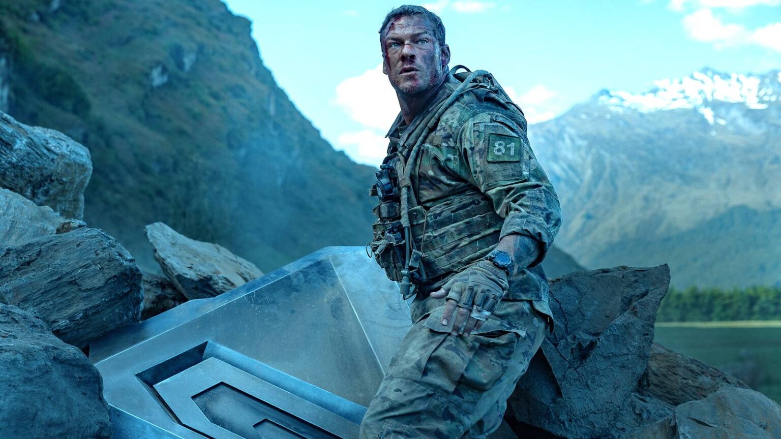 Alan ritchson s 81 standing next to part of the destroyed machine and looking beat up in war machine.jpeg